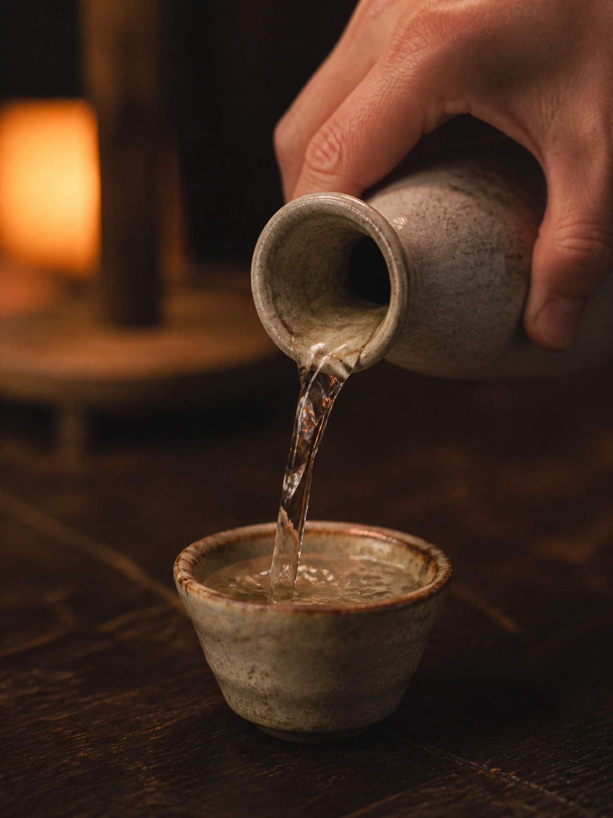 Rót sake từ tokkuri gốm vào ochoko dưới ánh đèn ấm