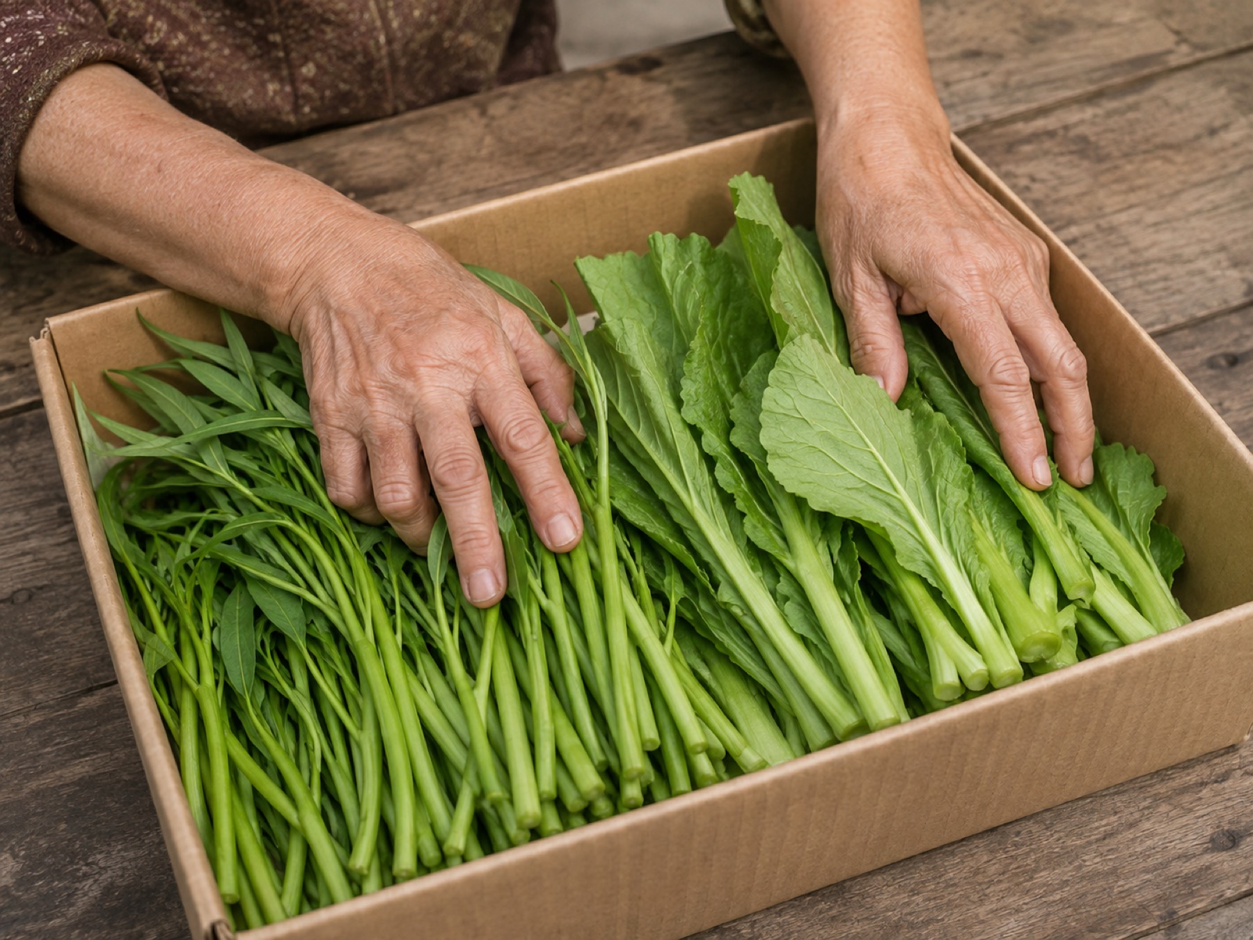 Hai bàn tay xếp rau muống và cải xanh vào thùng carton trên bàn gỗ