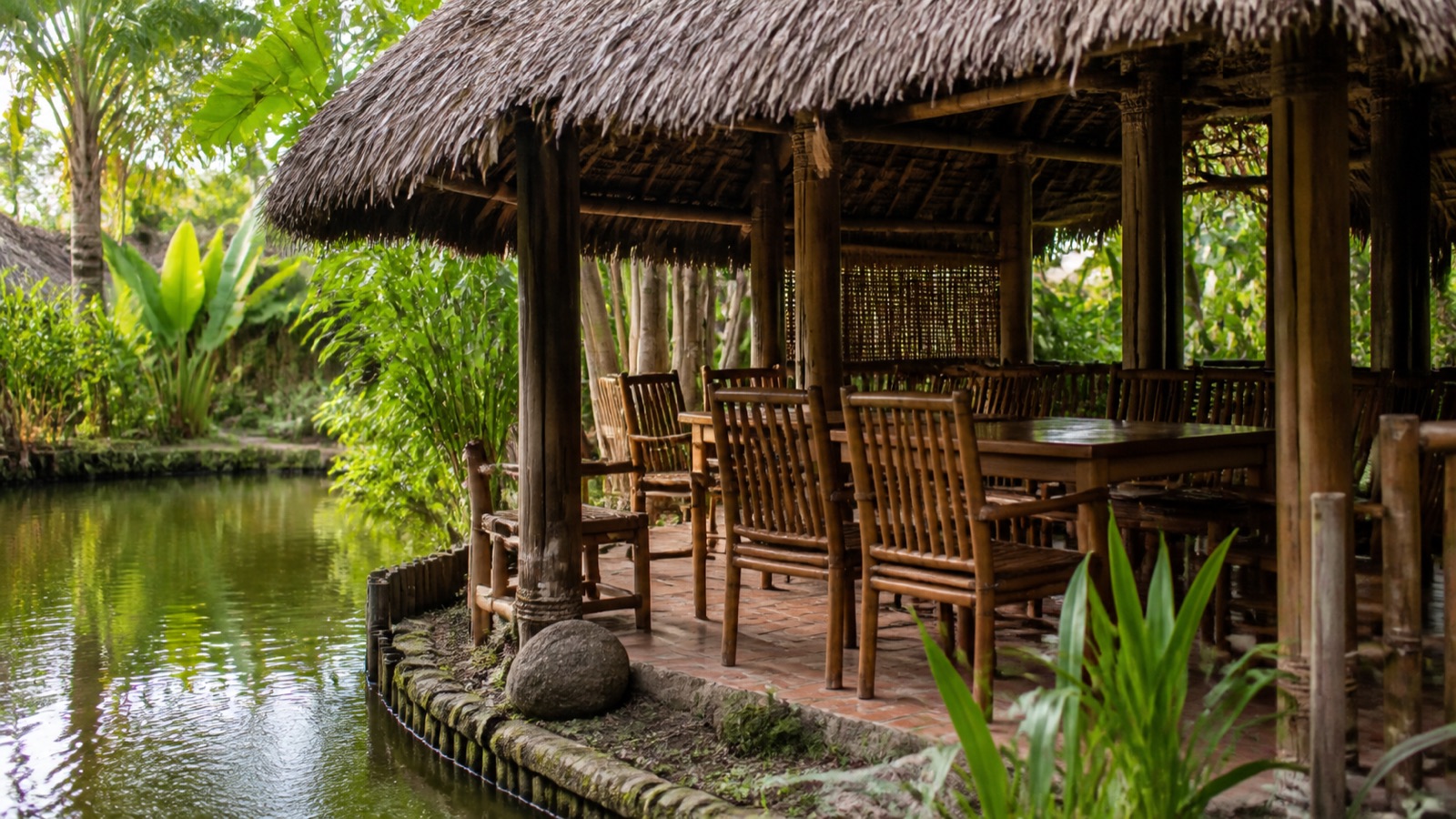Một chòi lá dựng sát mép ao, bàn ghế gỗ tre
