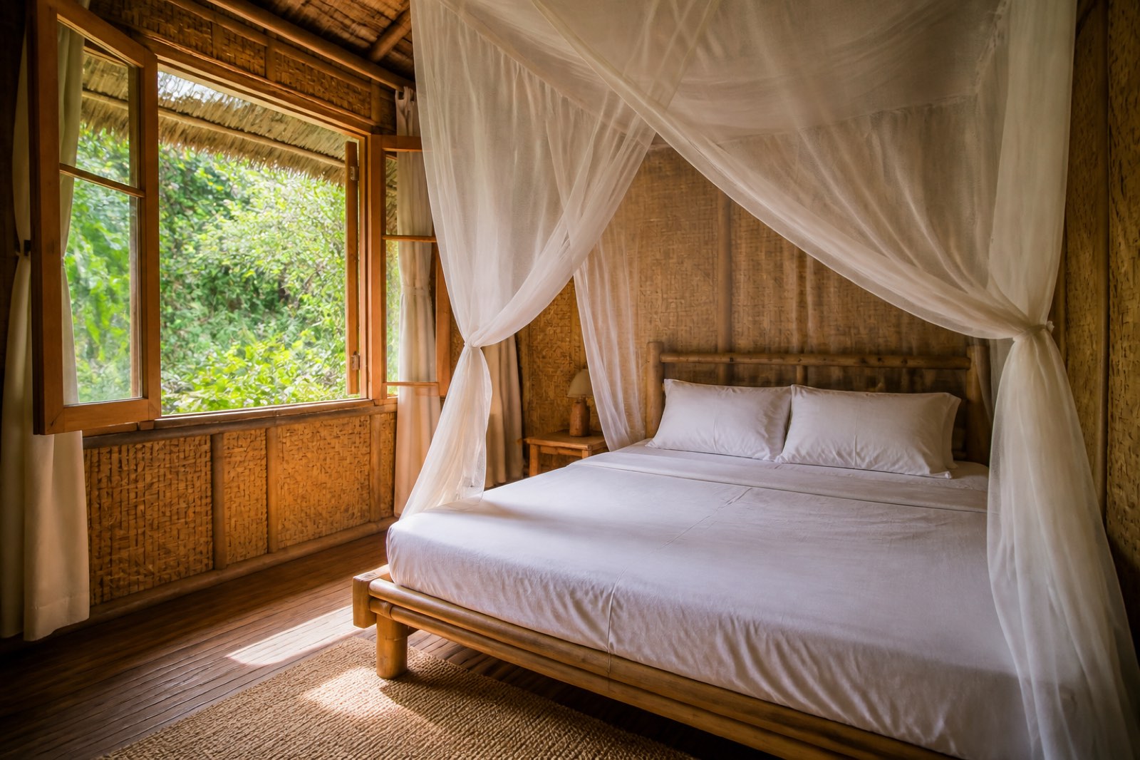 Nội thất bungalow tre: giường gỗ, màn tuyn, cửa sổ nhìn ra vườn