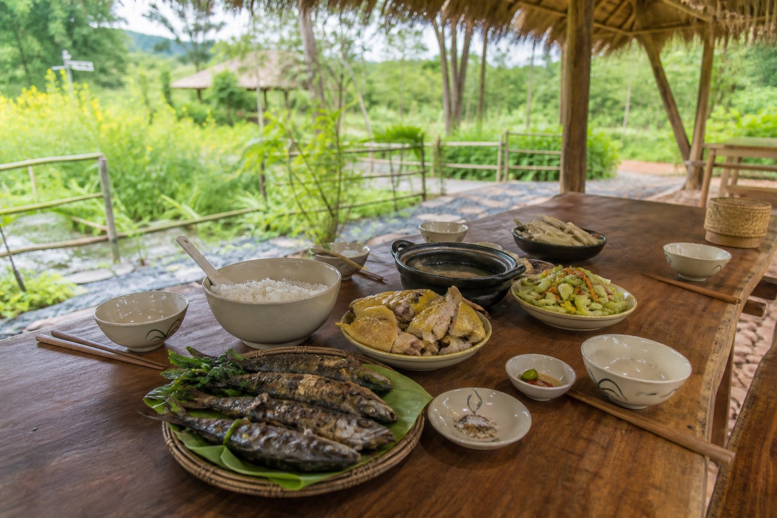 Bàn ăn ngoài trời dưới mái tranh với món ăn nông trại